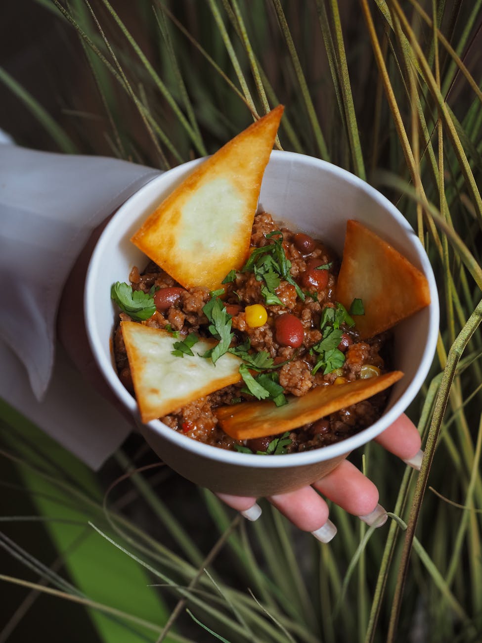 Bowl of chili con carne topped with tortilla chips and cilantro